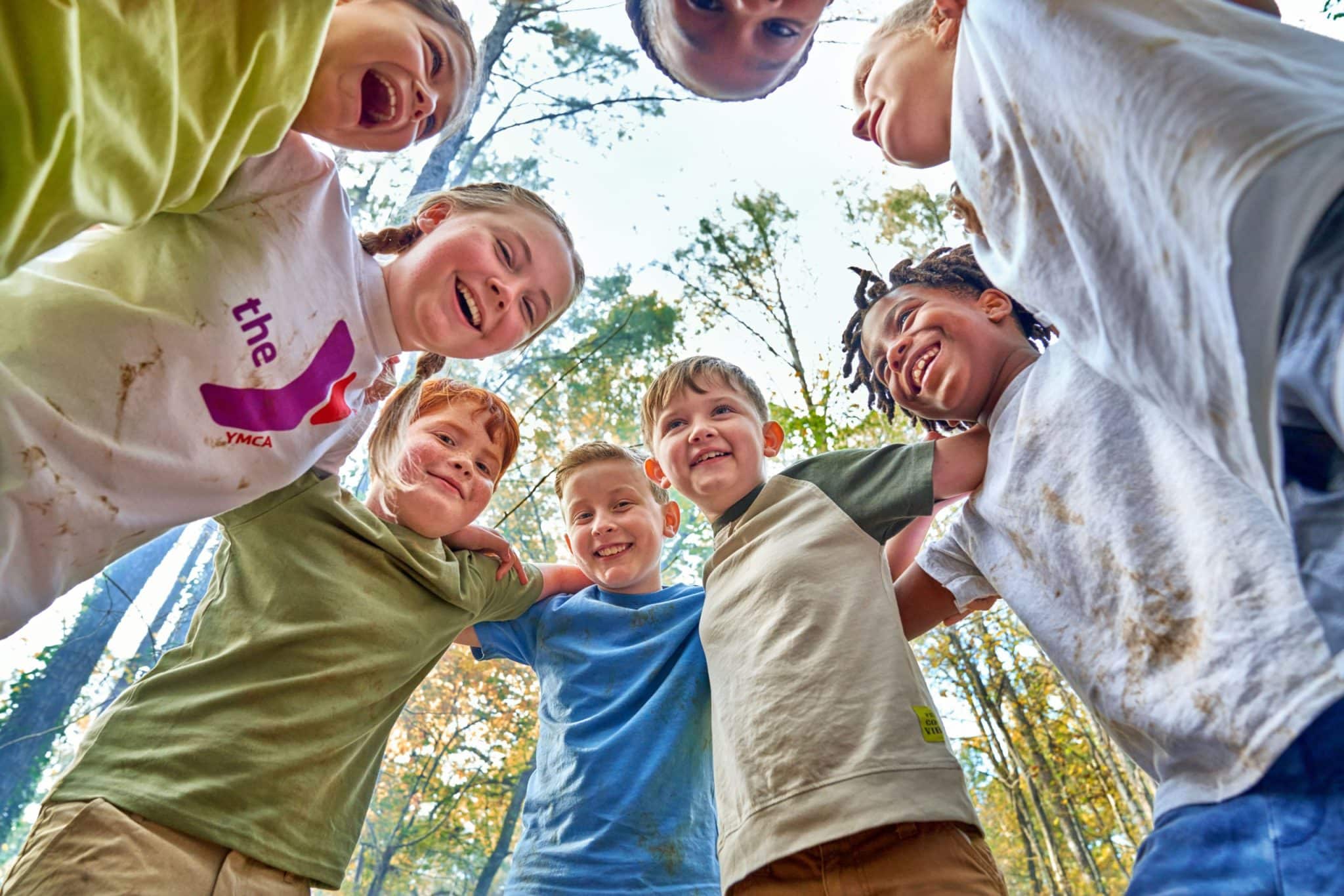 This image captures a group of children enjoying a playful moment outdoors. They are standing in a circle, looking down towards the camera, which gives a unique