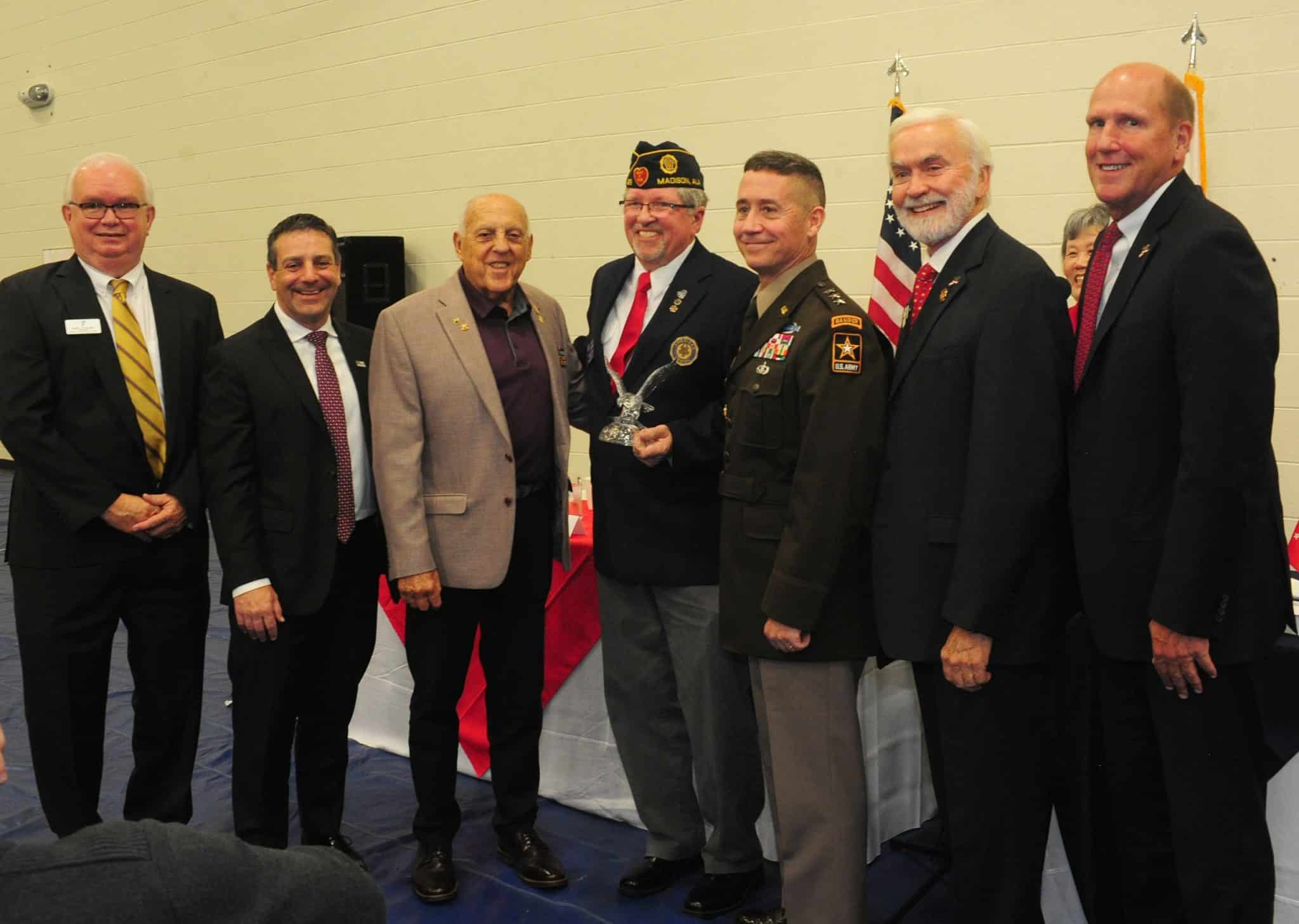 The image presents a group of seven men posing together at what appears to be a formal event. The men vary in age and are dressed in a mix