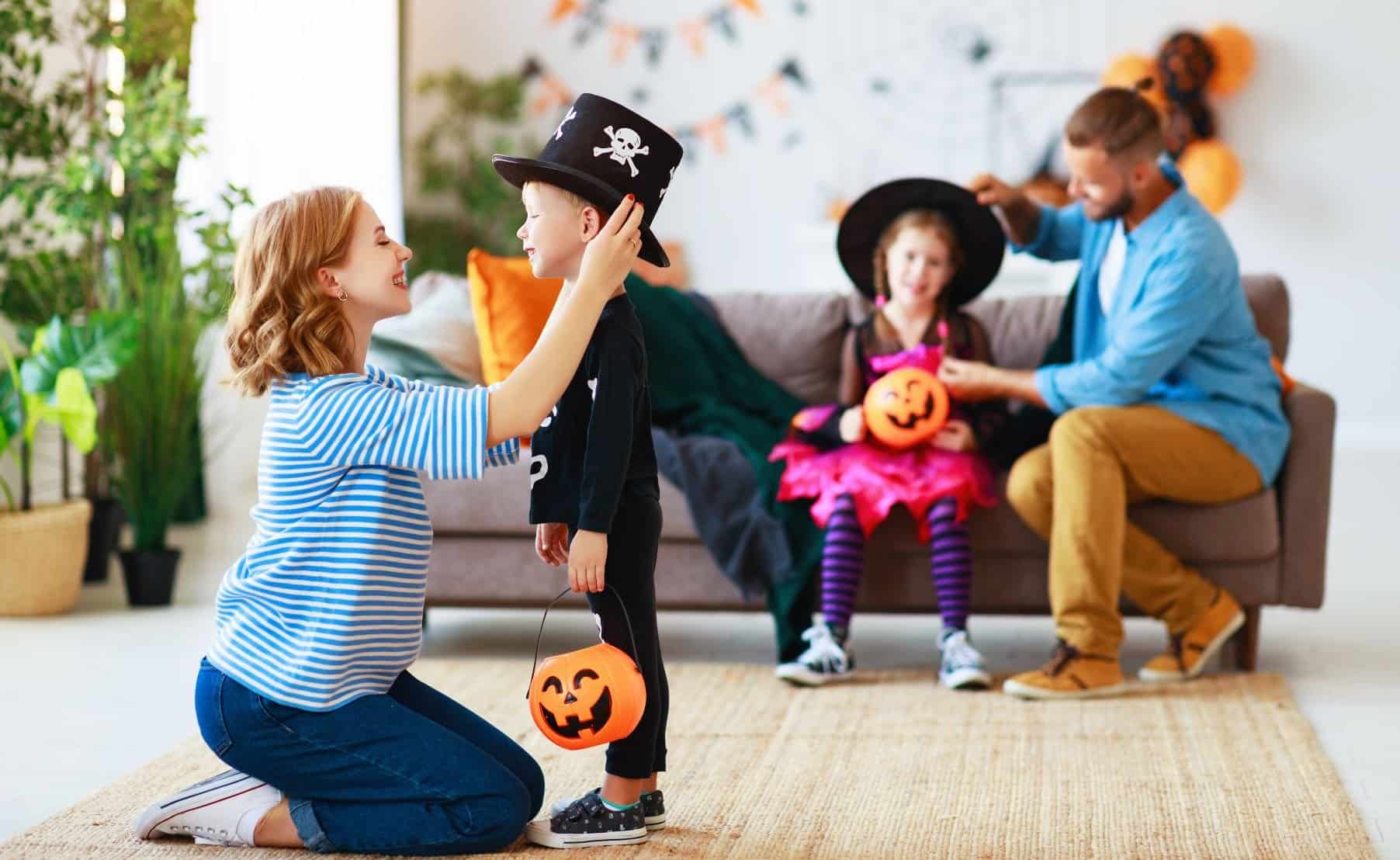 This image captures a joyful family scene during a Halloween celebration. On the left side of the photo, a woman dressed in a blue and white striped shirt