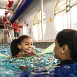 This image captures a joyful swimming lesson scene in an indoor pool.